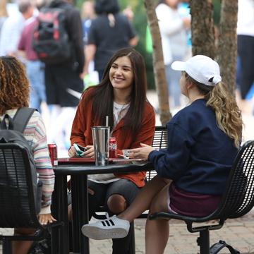 Three women sit at a picnic table to visit.